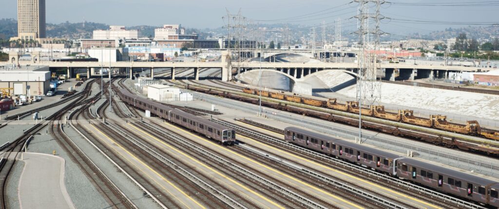 View of Division 20 Portal Widening & Turnback Facility Project tracks, vehicles with LA River and city in background.