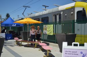 Two women standing in a seating area with benches and sun umbrellas adjacent to a light rail train